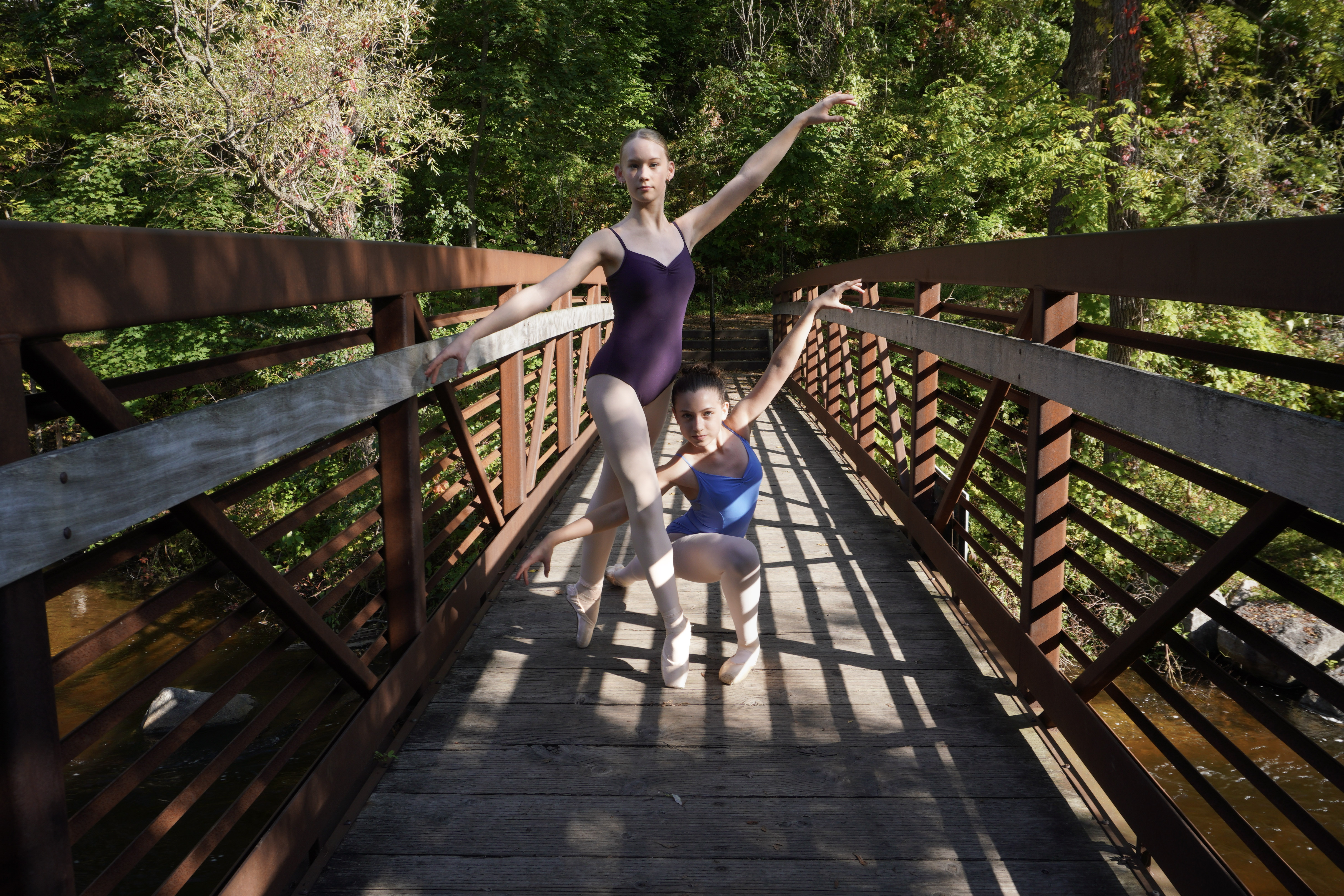 two female dancers in a purple and blue leotard pose outside on a bridge